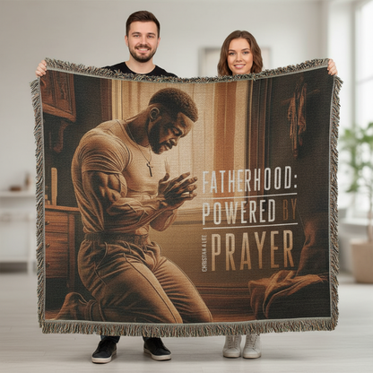 Two people holding a blanket with a printed design of a man praying and text 'Fatherhood: Powered by Prayer'.