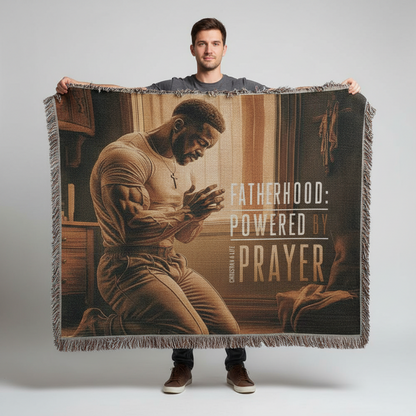 Man holding a blanket with a printed design of a man praying and text 'Fatherhood: Powered by Prayer'.